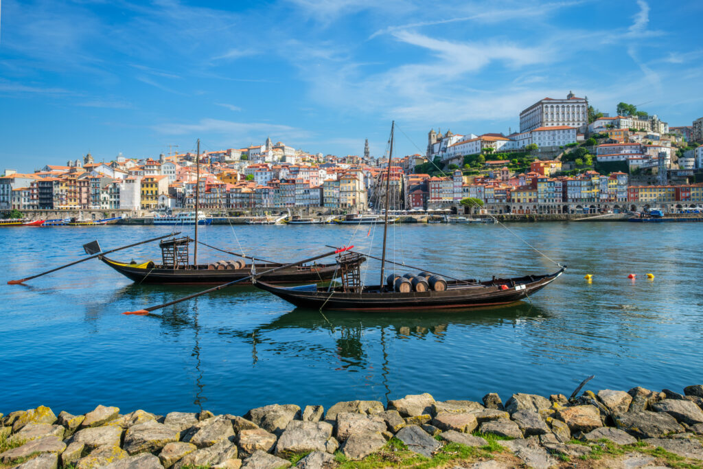 View of Porto city and Douro river with traditional boats with port wine barrels from famous tourist viewpoint Marginal de Gaia riverfront. Porto, Vila Nova de Gaia, Portugal