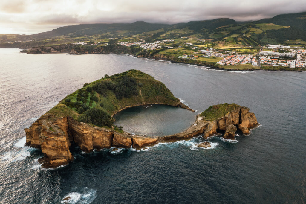Majestic aerial view of round shaped island in sea located near Vila Franca do Campo under cloudy sky